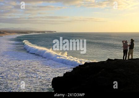 Coppia su una scogliera che guarda la vista su rulli e onde che si infrangono a El Cotillo, Fuerteventura, Isole Canarie, Spagna, Europa. Febbraio 2024 Foto Stock