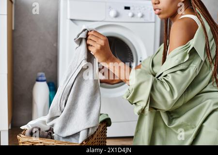 Una donna afroamericana con trecce afro viene vista asciugare i suoi vestiti in un cestino in un bagno. Foto Stock