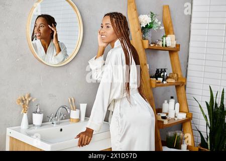 Una donna afroamericana con trecce afro si trova di fronte a uno specchio in un bagno moderno Foto Stock