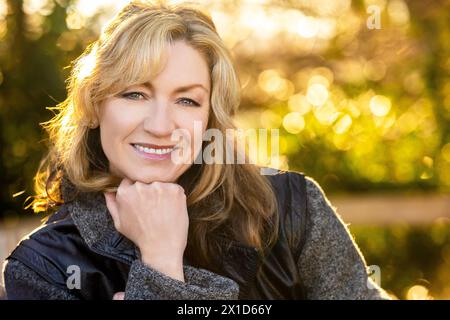 Attraente donna sorridente di mezza età all'aperto che riposa sulla mano e si illumina dal caldo sole al tramonto o all'alba Foto Stock