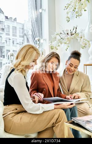 Tre giovani donne si siedono su un divano, infilate in un tablet, discutono dei dettagli del matrimonio e fanno acquisti per il grande giorno. Foto Stock