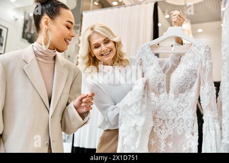 Due giovani donne valutano attentamente un abito da sposa, discutendo i dettagli del design e la vestibilità perfetta per il giorno speciale. Foto Stock