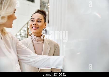 Due donne vestite elegantemente si stagliano l'una accanto all'altra, magari acquistando un abbigliamento da sposa. Foto Stock