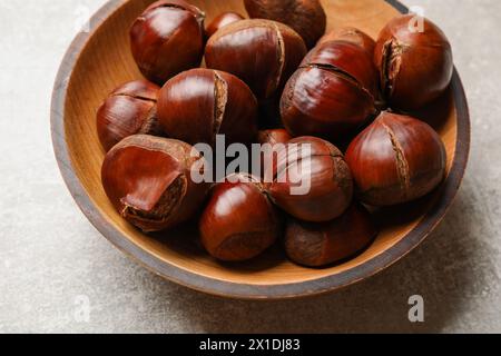 Castagne dolci fresche commestibili in una ciotola di legno su un tavolo grigio, primo piano Foto Stock