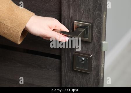 Donna che apre una porta di legno in interni, primo piano della mano sulla maniglia Foto Stock