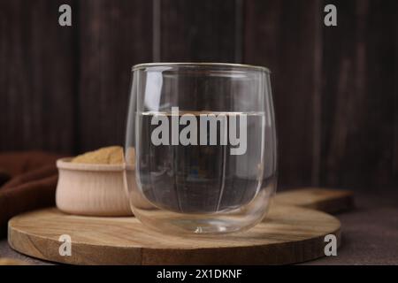 Fibra alimentare. Bicchiere d'acqua e polvere di buccia di psico su tavola marrone Foto Stock