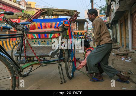 Due ciclisti di risciò gonfiano uno pneumatico a terra su un risciò a Varanasi, in India Foto Stock