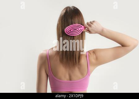 Vista posteriore della donna bruna che si pettina i capelli con una spazzola in plastica rosa. Foto Stock