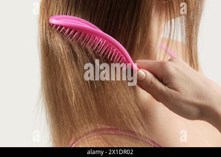 Cura dei capelli. Vista ravvicinata della donna bruna che pettina i capelli asciutti danneggiati con una spazzola in plastica. Foto Stock