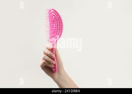 Giovane donna che tiene in mano una spazzola per capelli con detangler rosa, foto in studio Foto Stock