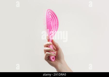 Giovane donna che tiene in mano una spazzola per capelli con detangler rosa, foto in studio Foto Stock