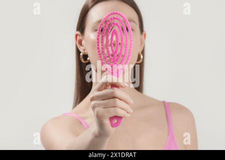 Giovane donna che tiene in mano una spazzola per capelli con detangler rosa, foto in studio Foto Stock