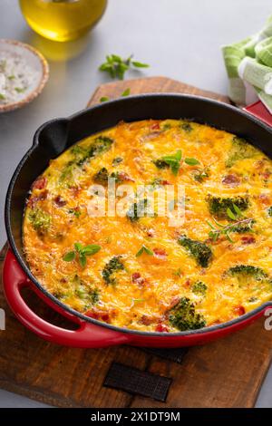 Frittata sana o quiche con broccoli e pepe rosso, condita con formaggio cheddar e pancetta intera in una padella di ghisa Foto Stock