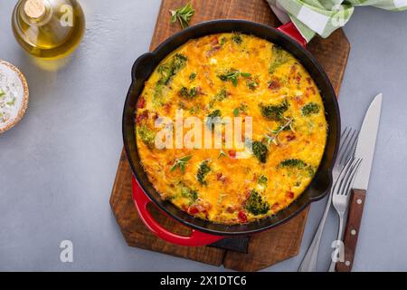 Frittata sana o quiche con broccoli e pepe rosso, condita con formaggio cheddar e pancetta intera in una padella di ghisa Foto Stock