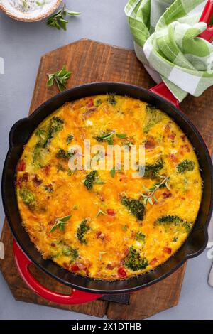 Frittata sana o quiche con broccoli e pepe rosso, condita con formaggio cheddar e pancetta intera in una padella di ghisa Foto Stock