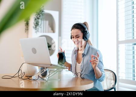 Donna che indossa le cuffie seduto a una scrivania che parla nel microfono e registra un podcast Foto Stock