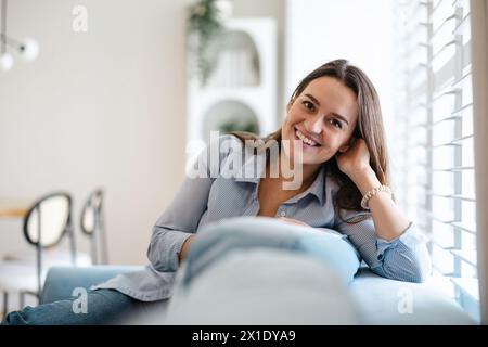 Ritratto di un sorridente giovane donna seduta sul divano di casa Foto Stock