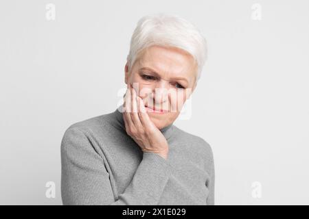 Donna anziana con guancia in dolore su sfondo grigio Foto Stock