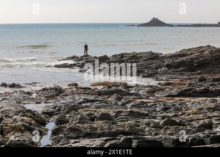 Pescatore solitario che pesca sulle rocce a Kenneggy Sand o Kenneggy Sands, una spiaggia remota nel sud-ovest della Cornovaglia, Inghilterra, Regno Unito Foto Stock