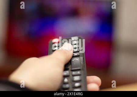 Una mano regge un telecomando davanti a un televisore, un gadget utilizzato per controllare apparecchiature elettroniche come dispositivi audio e video Foto Stock