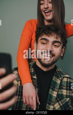 Immagine verticale di una coppia che indossa abiti casual che guarda lo schermo mobile mentre scatta una foto isoaltata su sfondo grigio. Foto Stock