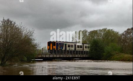 Un'alta marea primaverile riempie il fiume Douglas mentre un treno da Preston a Ormskirk attraversa il fiume avvicinandosi alla stazione di Rufford nel Lancashire occidentale. Foto Stock