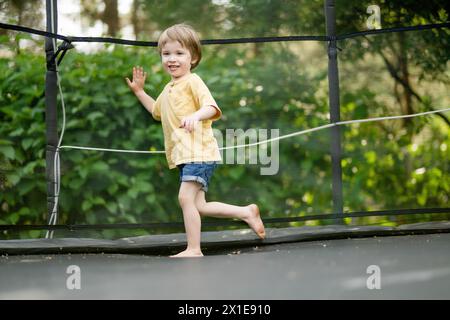 Un bambino carino che salta su un trampolino nel cortile di casa nelle calde e soleggiate giornate estive. Sport ed esercizi per bambini. Attività estive all'aperto Foto Stock