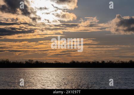 Tramonto sul lago con alberi in primo piano e cielo nuvoloso Foto Stock