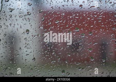 Una finestra con gocce di pioggia e un edificio rosso sullo sfondo Foto Stock
