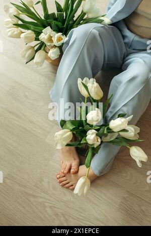 Una donna è seduta sul pavimento, tenendo in mano un mazzo di fiori. Foto Stock