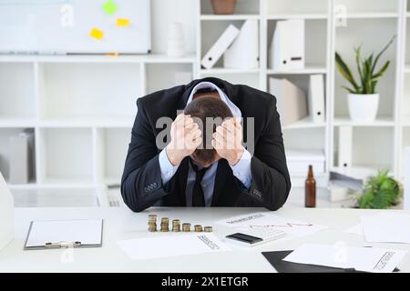 Uomo d'affari in bancarotta con pile di monete sul tavolo in ufficio Foto Stock