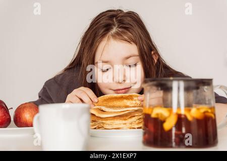 Bambina di pre-adolescenza, inala l'aroma di pancake appena sfornati impilati in una pila. Foto di alta qualità Foto Stock