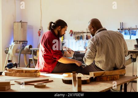 Carpenter che guarda i progetti degli schemi elettrici su laptop con software CAD con apprendista. Lavoratore di legno e collega che progettano mobili 3D personalizzati su notebook in studio, preparandosi per l'ordine del cliente Foto Stock