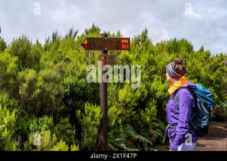 Descrizione: Turista femminile con zaino legge il cartello su un sentiero escursionistico verde cespuglioso. 25 Fontes Waterfalls, isola di Madeira, Portogallo, Europa. Foto Stock