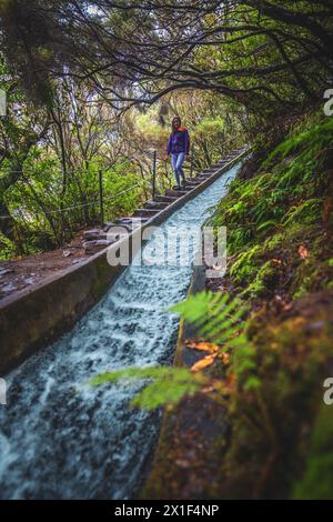 Descrizione: Turista femminile con zaino che scende le scale in un canale d'acqua curvo in pendenza ricoperto di rami laurali in una giornata di pioggia. 25 Fontes Foto Stock