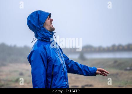 Descrizione: Vista laterale di un turista deluso che guarda in alto e tiene la mano sotto la pioggia. 25 Fontes, Mad Foto Stock