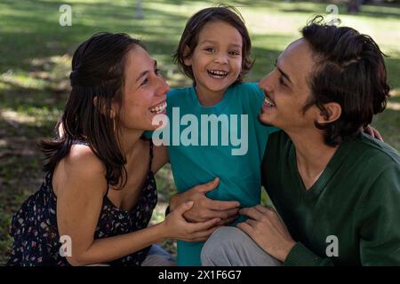 I giovani genitori latini condividono felicemente con il loro figlio di 3 anni al parco. Concetto di famiglia. Foto Stock