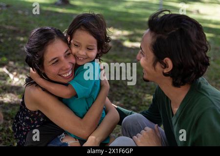 I giovani genitori latini condividono felicemente con il loro figlio di 3 anni al parco. Concetto di famiglia. Foto Stock