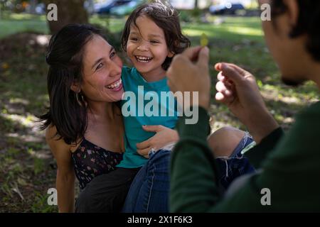 I giovani genitori latini condividono felicemente con il loro figlio di 3 anni al parco. Concetto di famiglia. Foto Stock