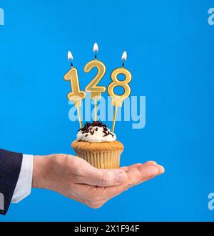 Cupcake per il compleanno a mano - candela numero 128 su sfondo blu Foto Stock