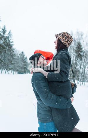 Bella coppia giovane ed elegante che si diverte nel Winter Snowy Park. Un giovane tiene la sua ragazza tra le braccia e si sta divertendo Foto Stock