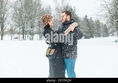 Felice, bella, giovane e divertente coppia di amanti in abiti invernali alla moda che ballano in Un parco con la neve. Amore, sentimenti e danza Foto Stock