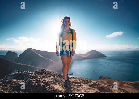 Descrizione: Vista frontale ad angolo basso di una donna backpacker che cammina in cima alle colline pedemontane di un'isola nell'Oceano Atlantico al mattino. São Lourenceo Foto Stock