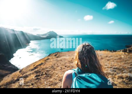 Descrizione: Vista a spalla di una turista che cammina giù per una collina che domina il paesaggio costiero e l'Oceano Atlantico. São Lourento, Madeira ISL Foto Stock