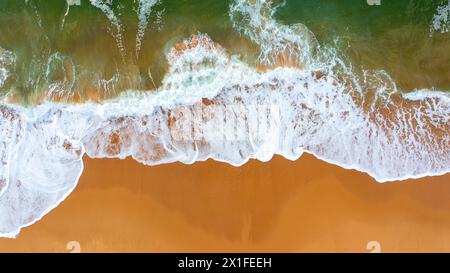 Vista da drone di splendidi filmati senza interruzioni mentre le onde turchide del mare si infrangono sulla costa sabbiosa. Scatto aereo di spiaggia dorata che incontra acque blu profonde dell'oceano e onde schiumose Foto Stock