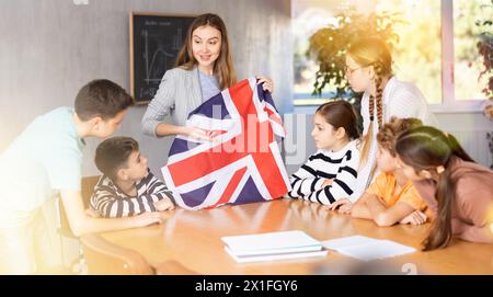 Insegnante donna positiva che discute con studenti preadolescenti bandiera di stato della Gran Bretagna in udito della scuola media Foto Stock