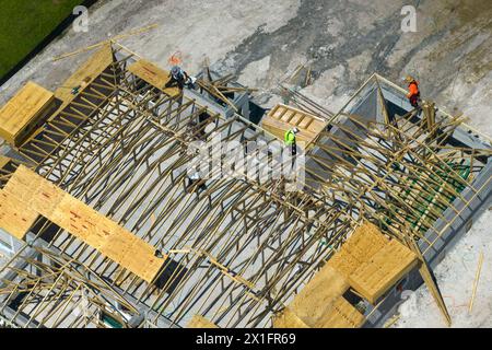 Veduta aerea dei costruttori che lavorano su una casa residenziale non finita con struttura di telaio del tetto in legno in costruzione nella zona suburbana della Florida. Foto Stock