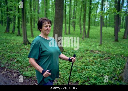 Una donna anziana è impegnata nel nordic walking con bastoni nella foresta primaverile Foto Stock