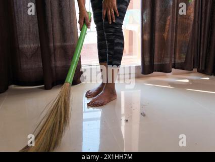 Una donna con un abbigliamento casual spazza efficacemente il pavimento con una scopa, contribuendo a creare un ambiente domestico pulito e organizzato Foto Stock