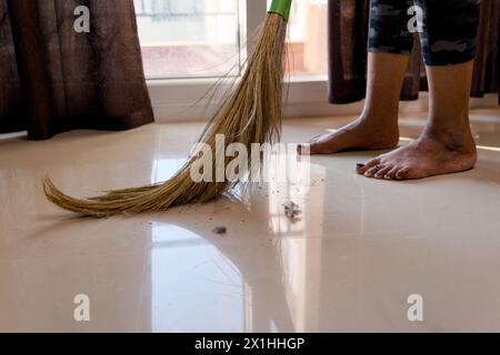 Una donna concentrata spazza il pavimento con una scopa, mantenendo il suo spazio abitativo pulito e organizzato. Foto Stock